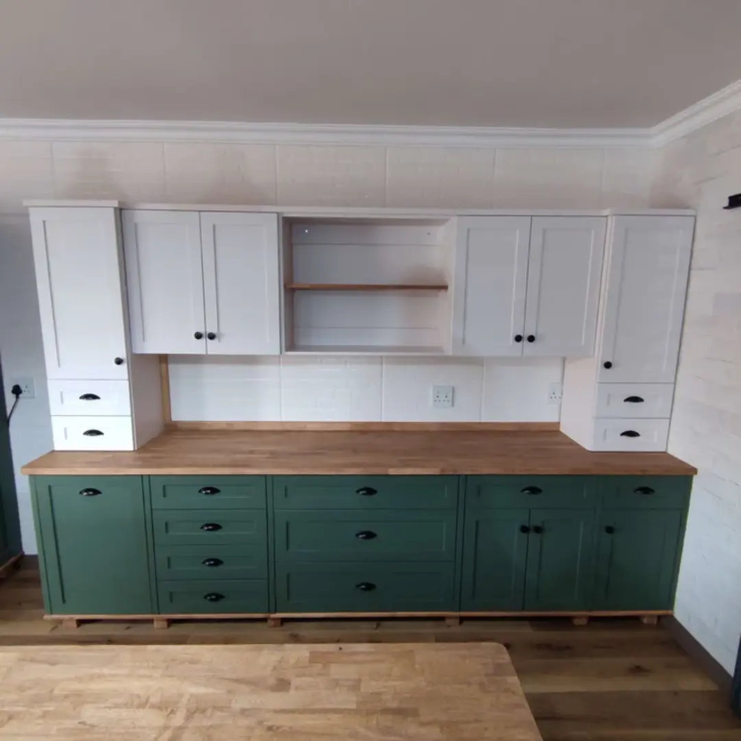 Two-tone kitchen cabinetry with white upper cabinets, green lower cabinets, black cup handles, and a wooden countertop against a white tiled wall.