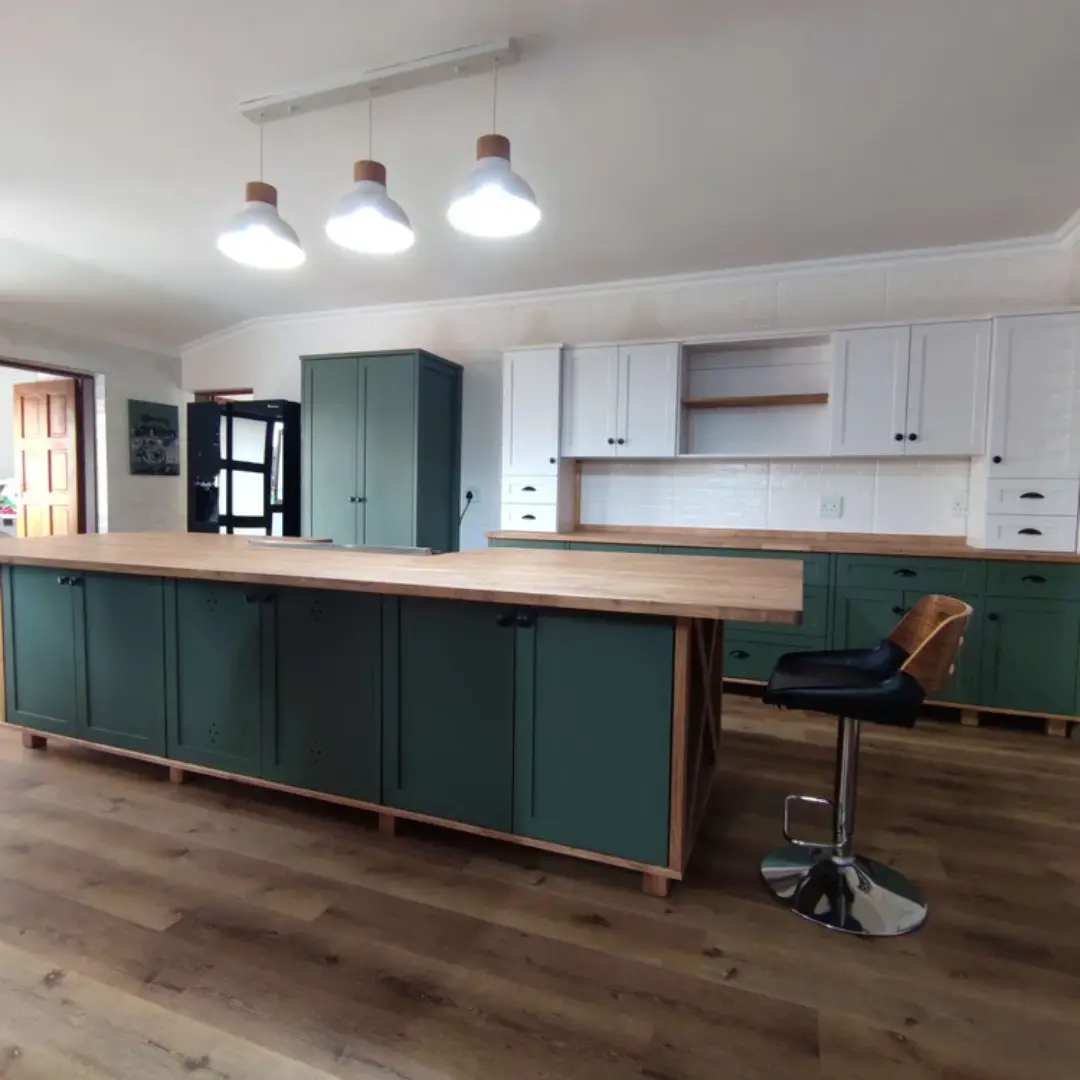 Spacious kitchen with a large wooden island featuring green shaker-style cabinets, matching green pantry unit, white upper cabinets, wooden countertops, and trio pendant lighting.