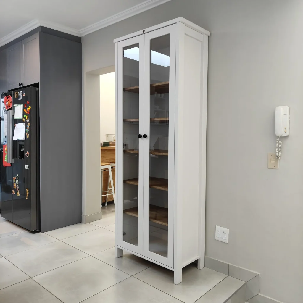 Tall white display cabinet with glass doors and wooden shelves in a modern kitchen.