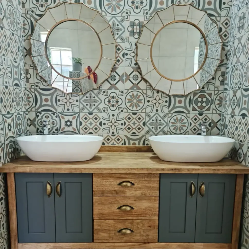 Bathroom vanity with wood countertop, dark cabinets, two vessel basins, and round mirrors on patterned tile walls.