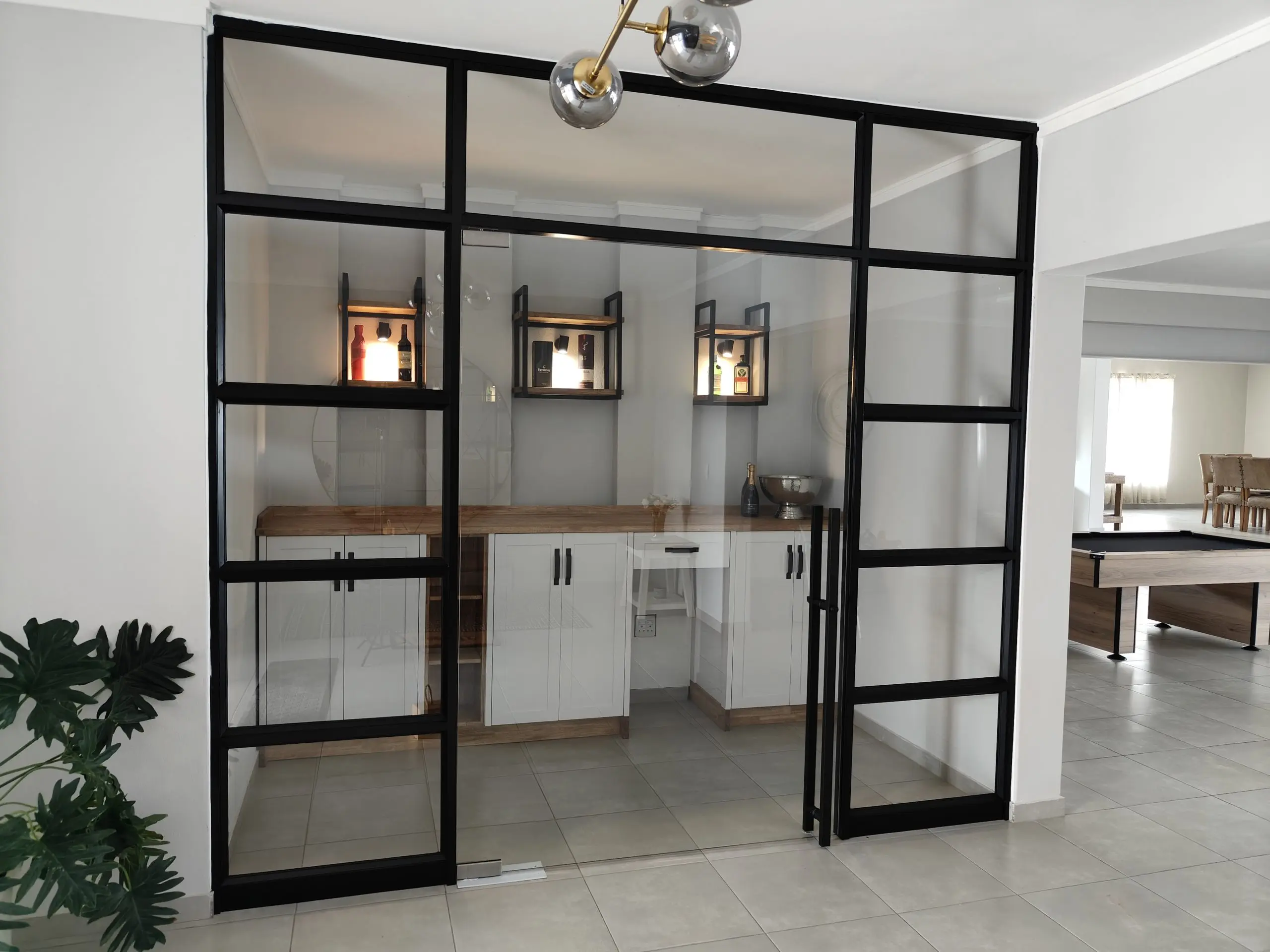 Modern home bar area with white cabinets, wood countertop, and black-framed glass doors.