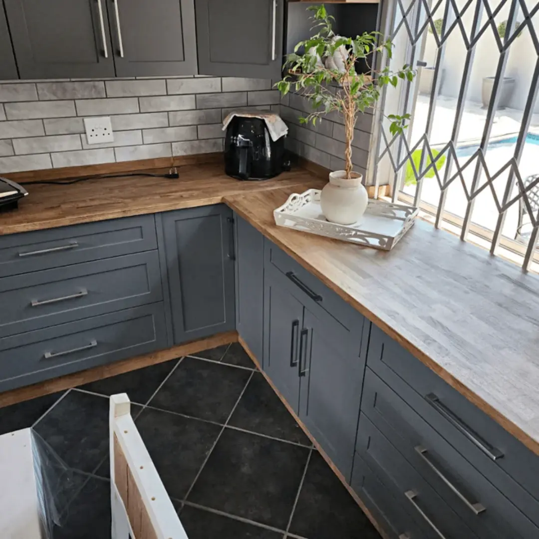 Grey shaker-style kitchen cabinets with stainless steel handles, wood countertop and light grey subway tile backsplash.