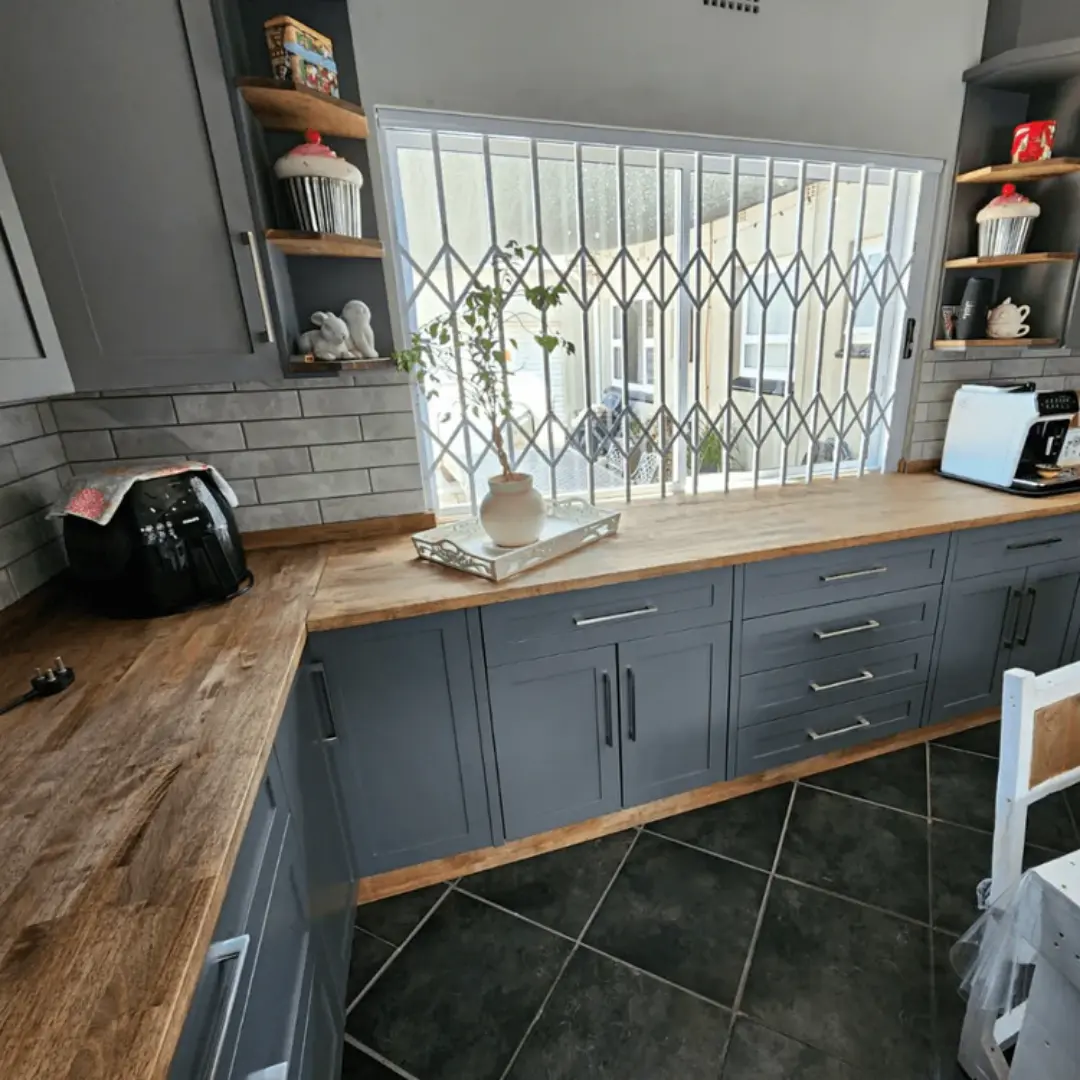 Grey shaker-style kitchen cabinets with stainless steel handles, wood countertop and light grey subway tile backsplash.